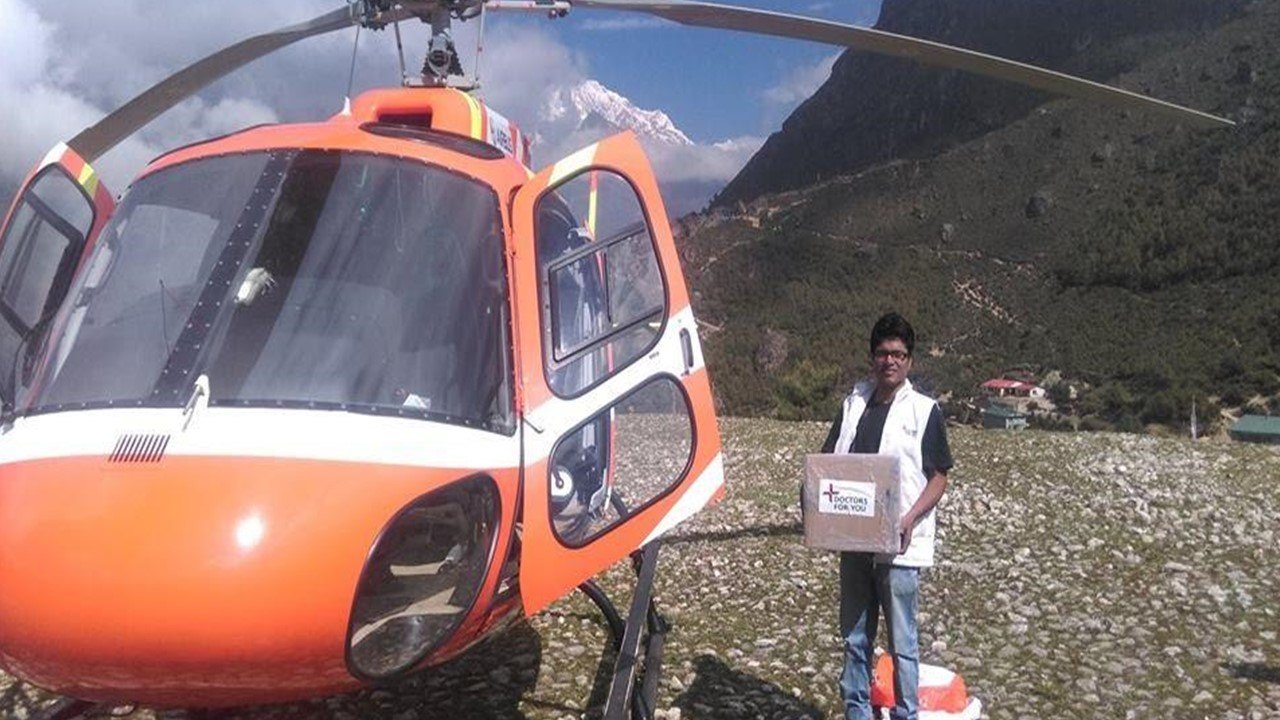 A DFY volunteer with medical supplies beside a relief helicopter in the Himalayas